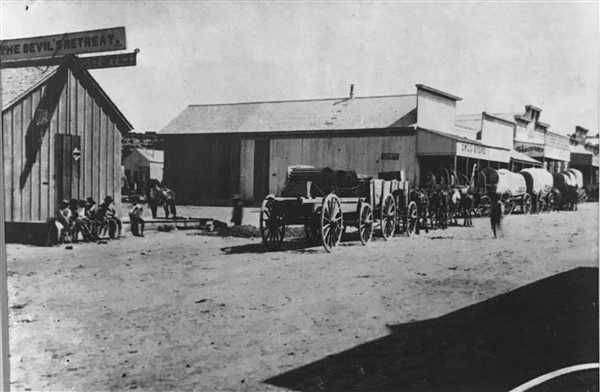 An old image of a town with horse drawn carriages.
